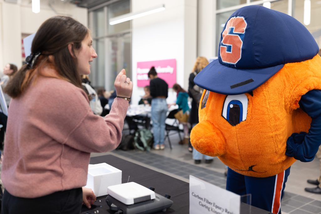 Otto the orange at a research symposium looking at a students research project