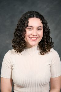 Headshot of Ayla, she is in front of a dark background wearing a light colored sweater