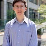 Headshot of Edward in front of a building, wearing a light colored dress shirt