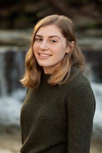 Headshot of Emerson in front of a blurred background, she is wearing a dark sweater