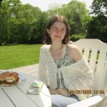 Taryn is wearing a green and white top sitting at a table, she is sitting in front of a small field and trees