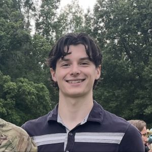Photo of Owen, he is in front of a group of trees and wearing a dark blue collared shirt
