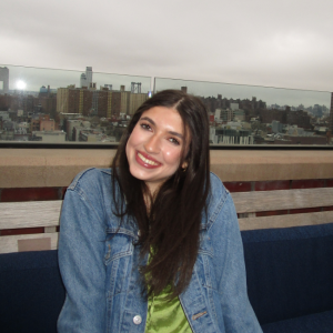 Photo of Mary in front of a city skyline, she is wearing a denim jacket and smiling